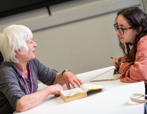 A student and teacher sat opposite each other at a table, discussing work