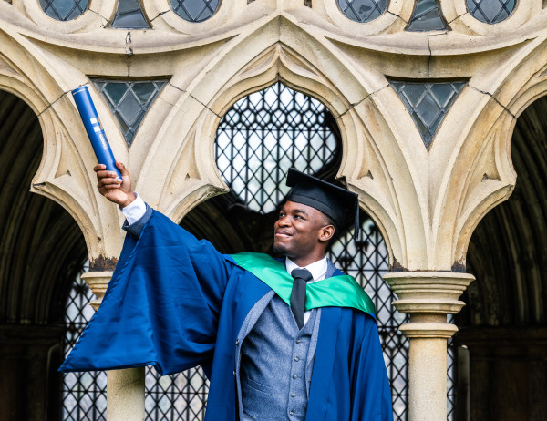 A Higher Education student at graduation, holding their certificate up outside the Cathedral.