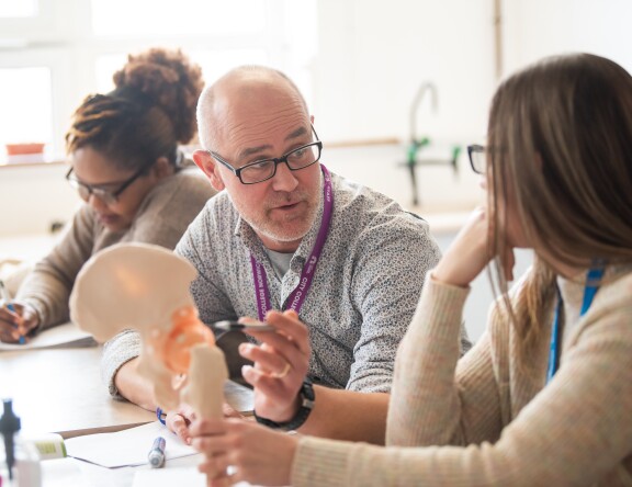 A teacher and student in discussion, with the teacher holding an anatomical model.