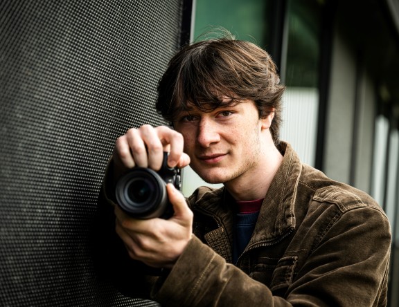 Close-up of a student with a camera in their hand, holding the camera as if about to take a photo.