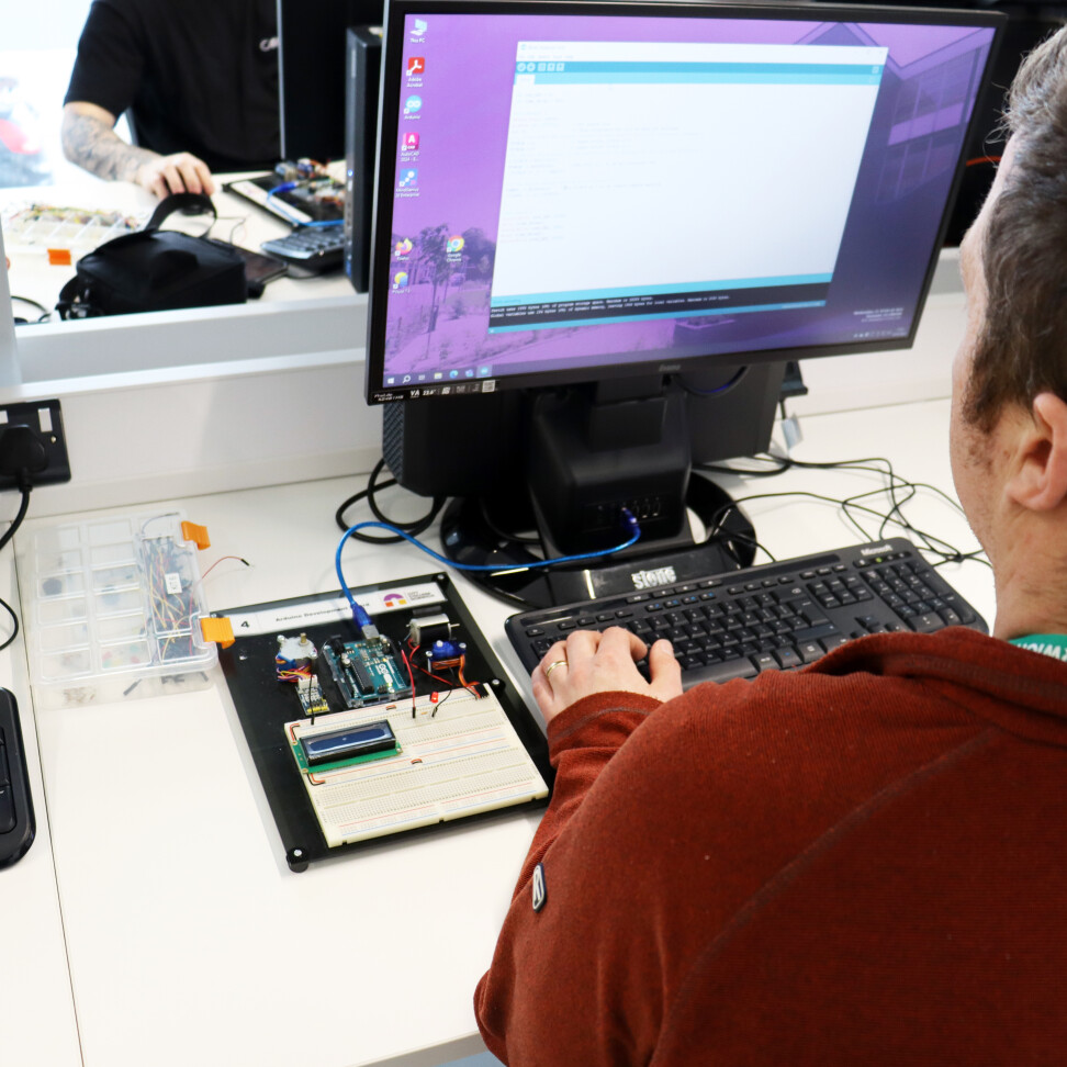 An Electrical and Electronic Engineering student sat with their back to the camera, typing at a computer.