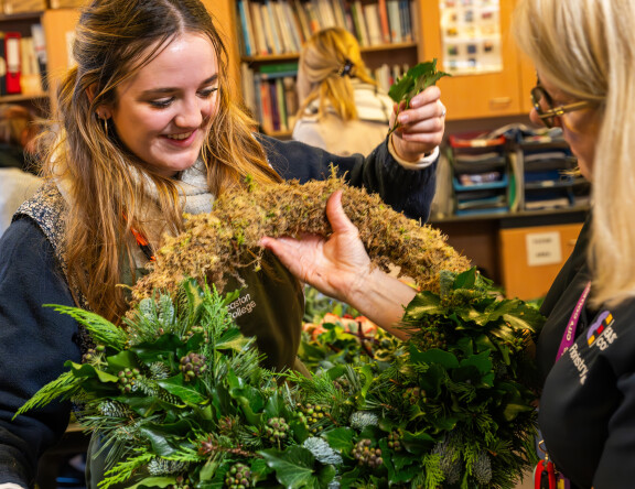 A student and teacher holding a wreath made of foliage.