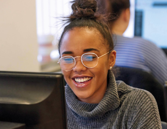 An Access to Higher Education student smiling, sat at their computer.