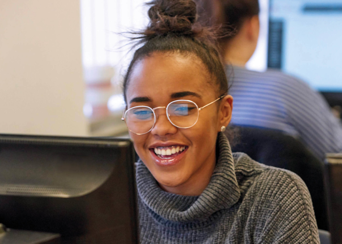 An Access to Higher Education student smiling, sat at their computer.