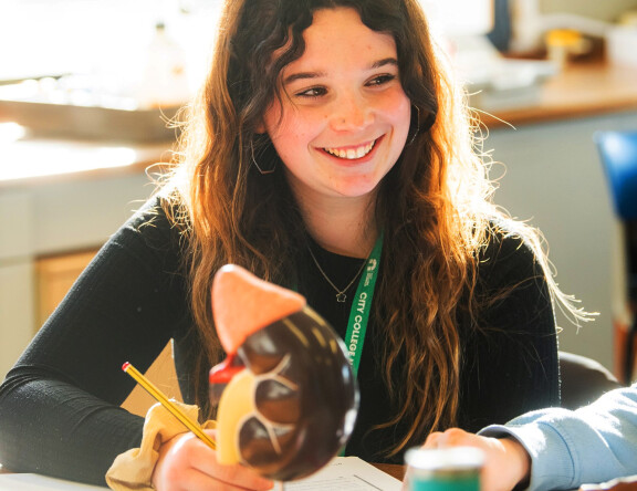 An Access to Higher Education: Science student sat at a table, smiling. They are sat in front of an anatomical model.