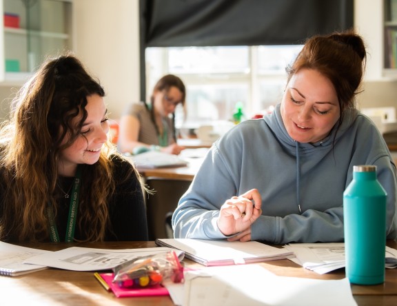 Two Access to Higher Education Science students are sat at a table, working. They are writing in notebooks.