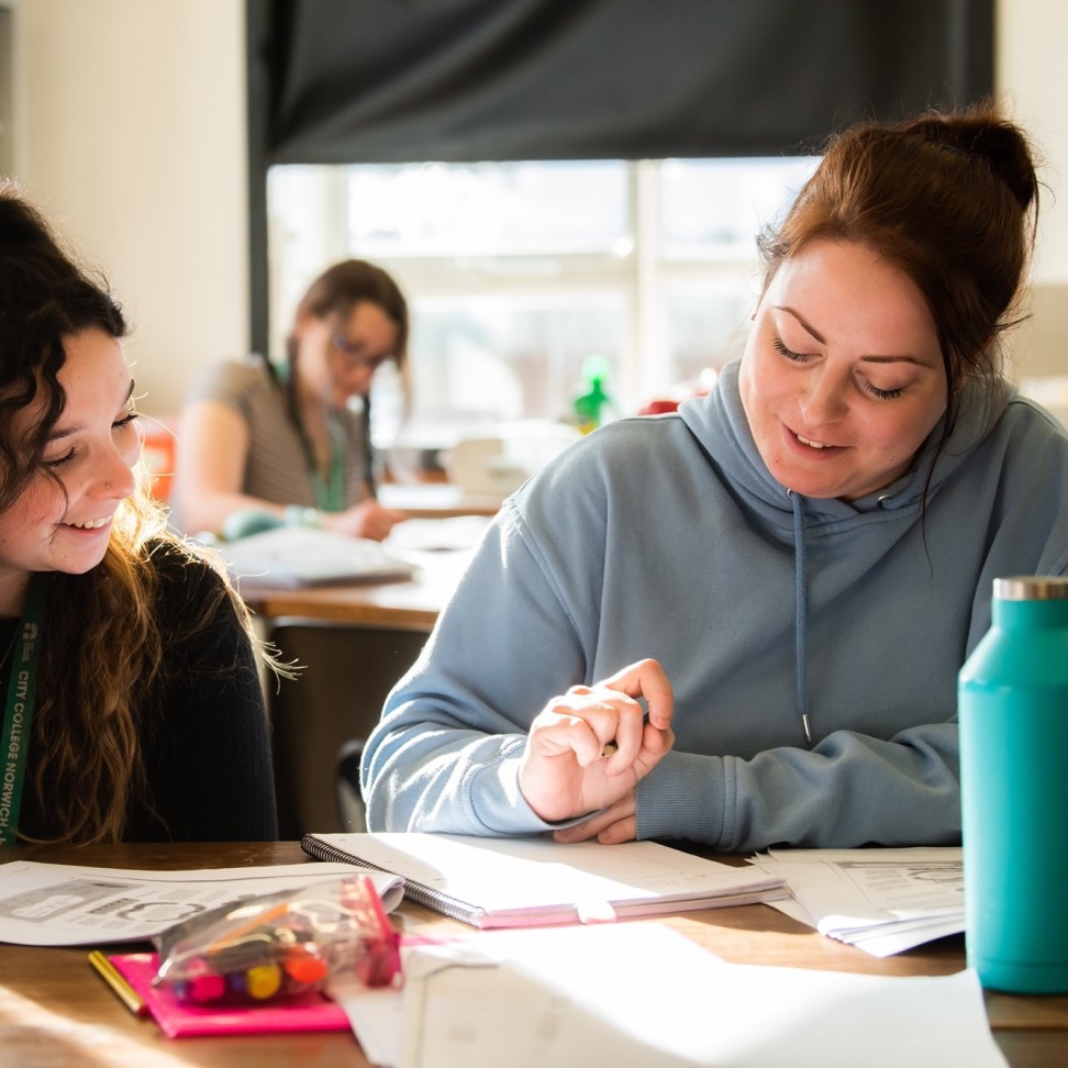 Two Access to Higher Education Science students are sat at a table, working. They are writing in notebooks.