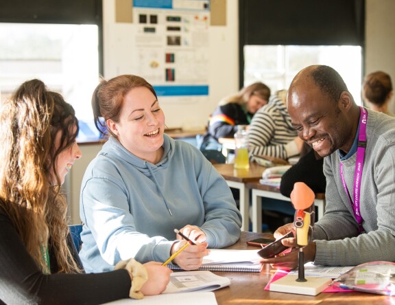 Two Access to Higher Education: Science students are sat at a table, with a teacher. A teacher is showing an anatomical model to the students.