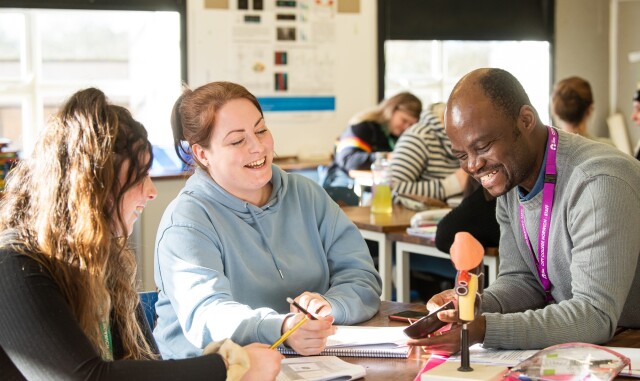 Two Access to Higher Education: Science students are sat at a table, with a teacher. A teacher is showing an anatomical model to the students.