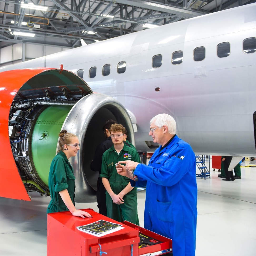 Two students are at the International Aviation Academy, They are standing in front of the Boeing 737, next to a teacher.