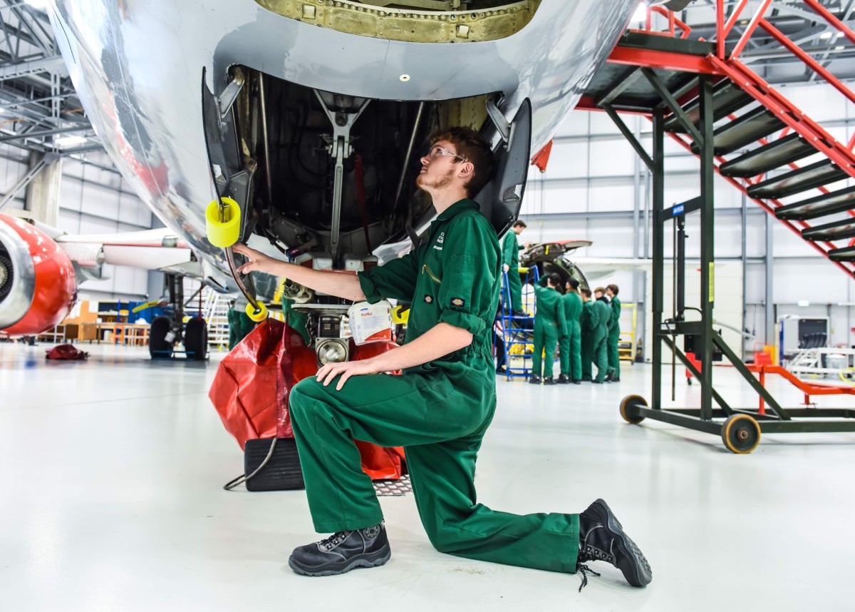 An Aviation student is kneeling under the body of a Boeing 737 plane, looking inside.