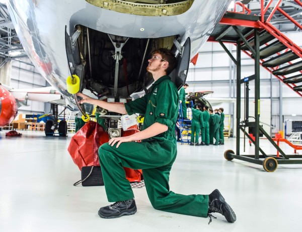 An Aviation student is kneeling under the body of a Boeing 737 plane, looking inside.