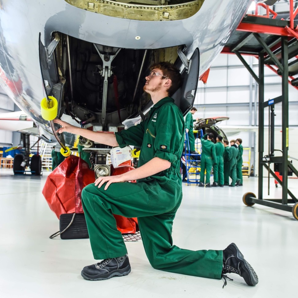 An Aviation student is kneeling under the body of a Boeing 737 plane, looking inside.