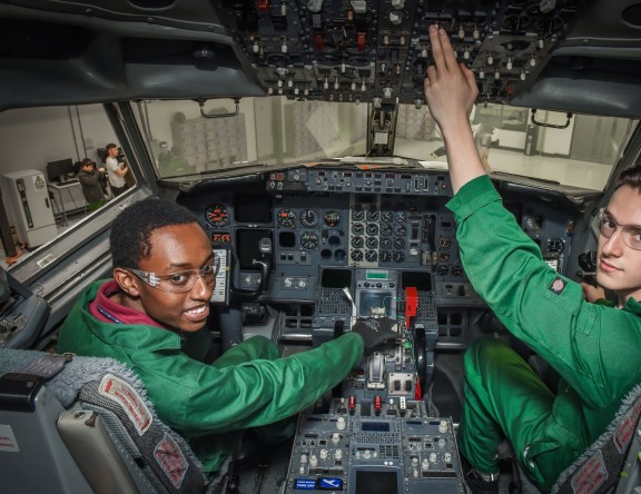 An Aviation student is sat in the control room of a Boeing 737 plane, smiling.