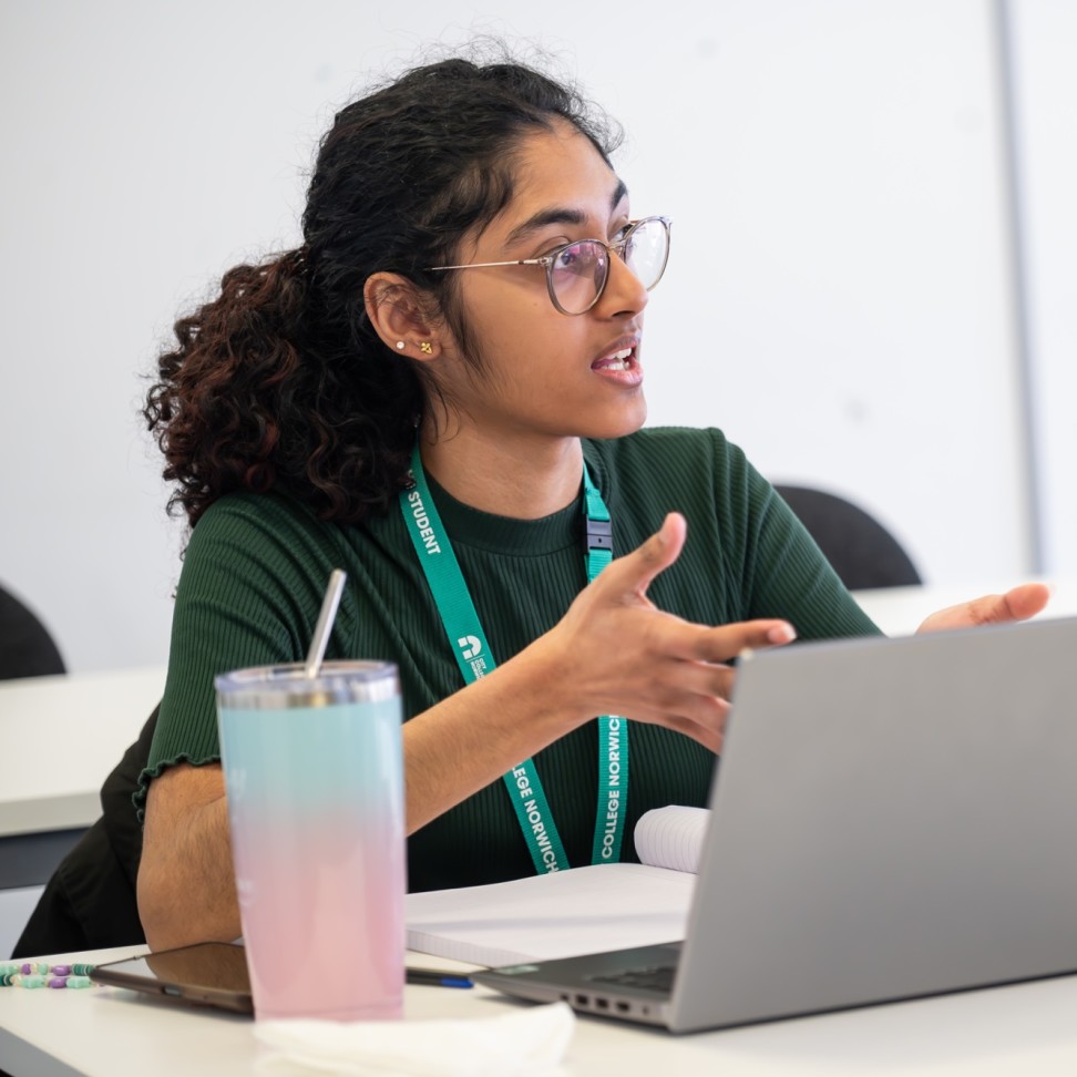 A Social Sciences student sits at a desk, with a laptop in front of them. They are talking to the class.