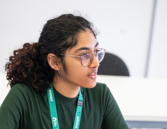 A Social Sciences student sat at a desk, with their laptop in front of them. They are looking towards the front of the class.