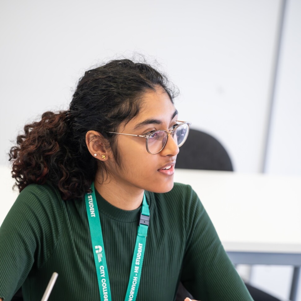 A Social Sciences student sat at a desk, with their laptop in front of them. They are looking towards the front of the class.