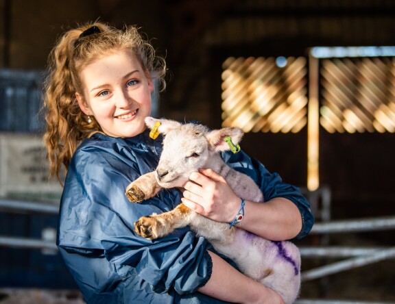 An Animal Science student is holding a lamb, and smiling.