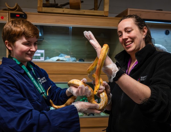 A Zoology student is holding a snake, with the assistance of a teacher. Both are smiling. 