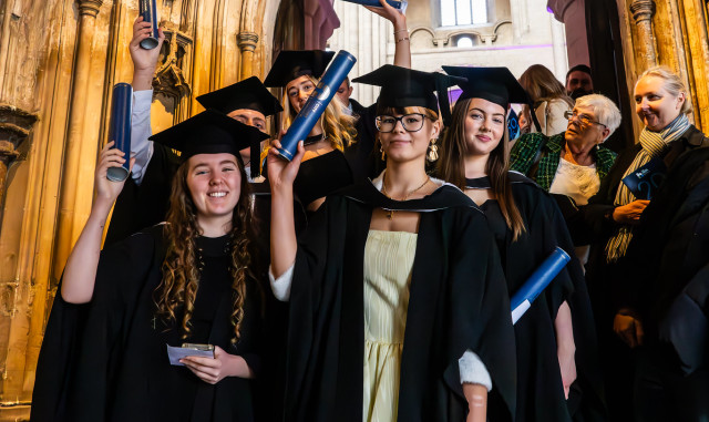 A group of graduates pose in the Cathedral, holding their certificates up.