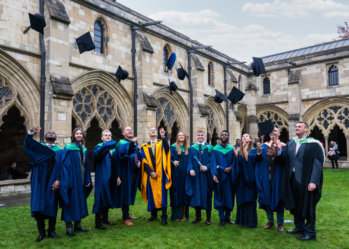 A group of graduates stand outside the Cathedral, throwing their caps in the air.