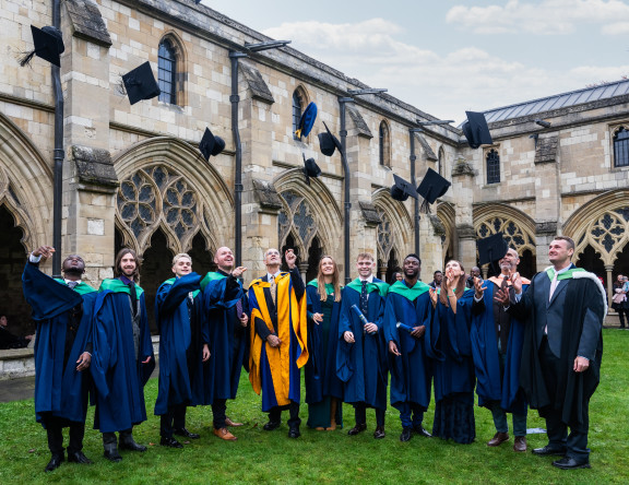 A group of graduates stand outside the Cathedral, throwing their caps in the air.